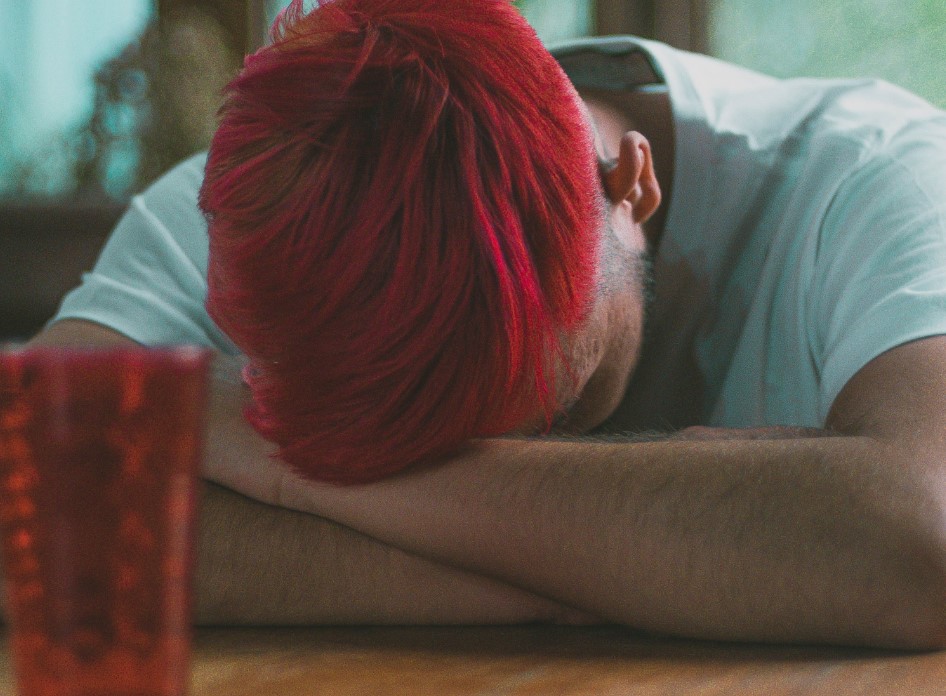 Man with head in arms, managing stress with cup on table