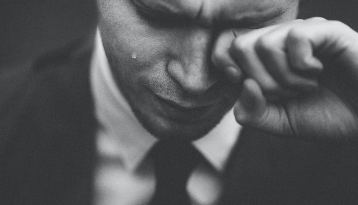 Man with tears running down side of face. one hand rubbing eye